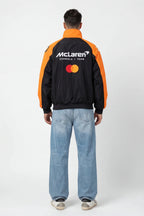 Black and orange McLaren Formula 1 Team bomber jacket with Mastercard logo, worn with jeans from revnhaus