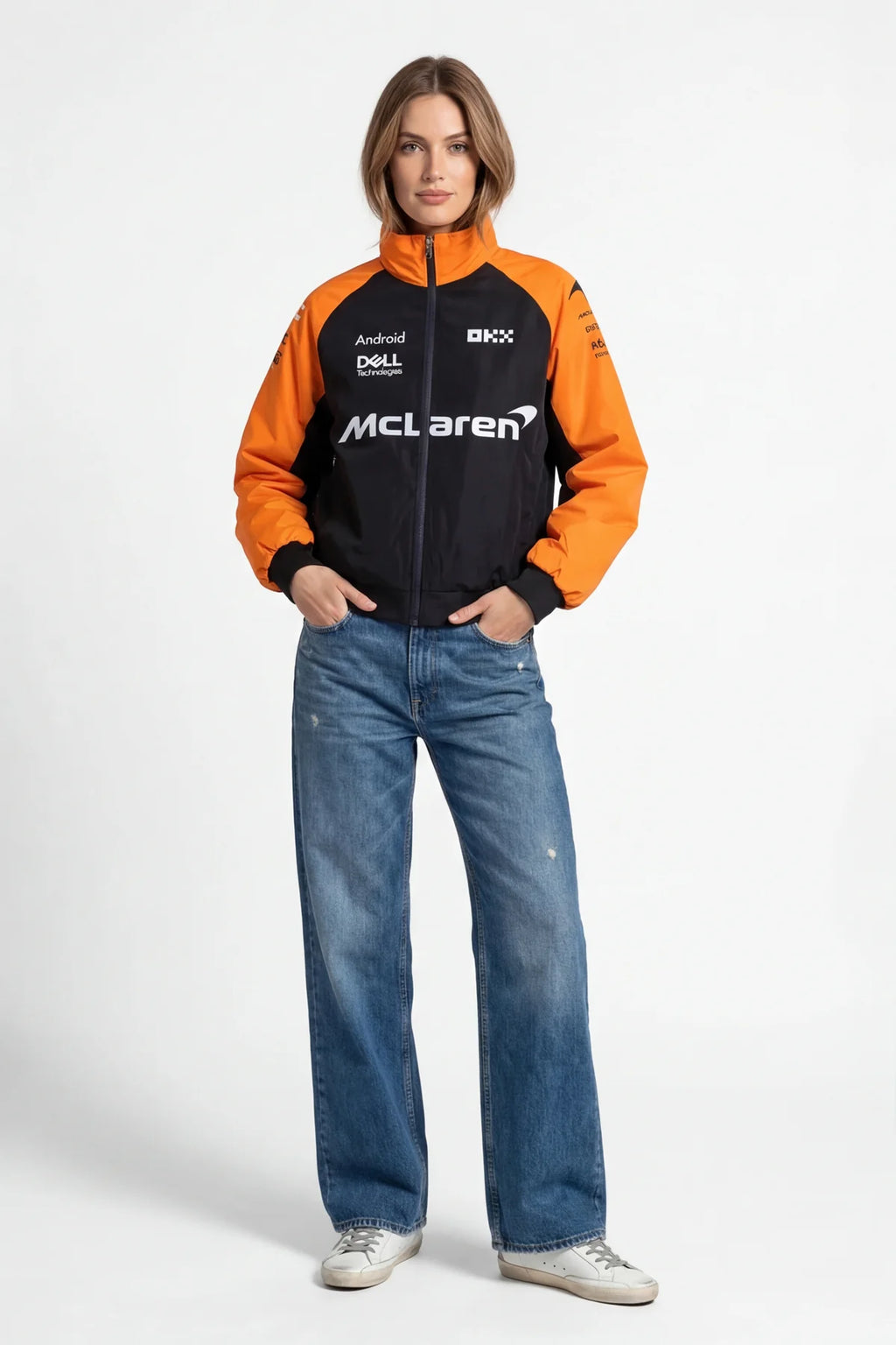 Woman wearing orange and black McLaren racing jacket with sponsor logos, paired with jeans from revnhaus