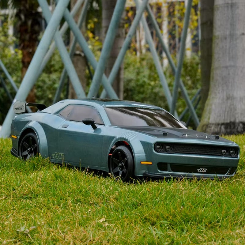 Teal RC drift car with black rims on grass, modern metal sculpture background from revnhaus