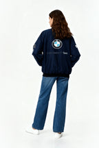 Woman wearing navy BMW Sauber F1 Team bomber jacket with logo, paired with jeans and white sneakers from revnhaus