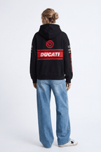 Black Ducati racing hoodie with red logo and sponsor patches, worn with jeans from revnhaus