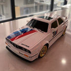 White BMW M3 E30 die-cast model with blue red stripes, gold wheels, and '30' livery from revnhaus
