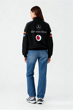 Black Mercedes-Benz racing jacket with Vodafone logo, worn with blue jeans and sneakers from revnhaus