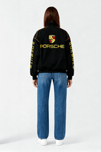 Black Porsche racing jacket with yellow logo and sleeve text, worn with blue jeans from revnhaus