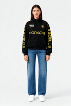 Black Porsche racing jacket with yellow lettering and logos, styled with jeans and sneakers from revnhaus