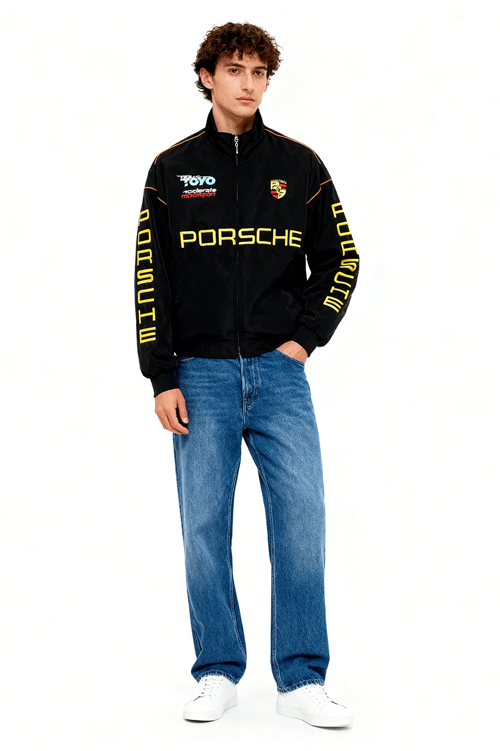 Black Porsche racing jacket with yellow logo and sleeve text, styled with jeans and white sneakers from revnhaus