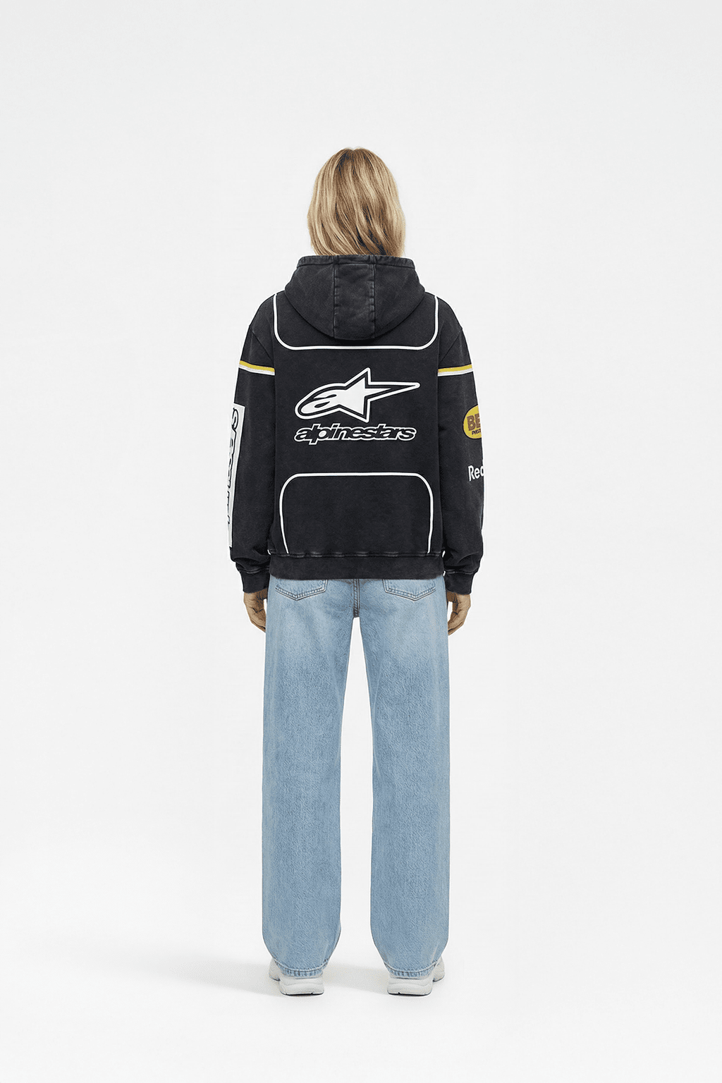 Black Alpinestars racing hoodie with white star logo and yellow stripes, worn with blue jeans from revnhaus