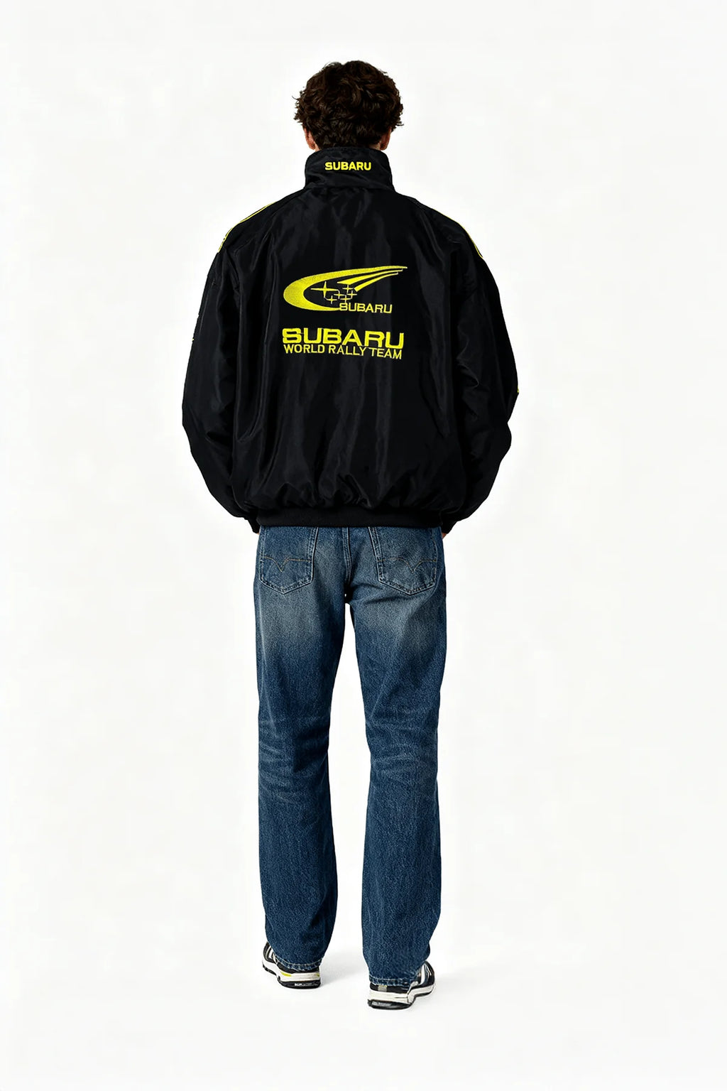 Black Subaru World Rally Team jacket with yellow logo, worn by model from behind, from revnhaus