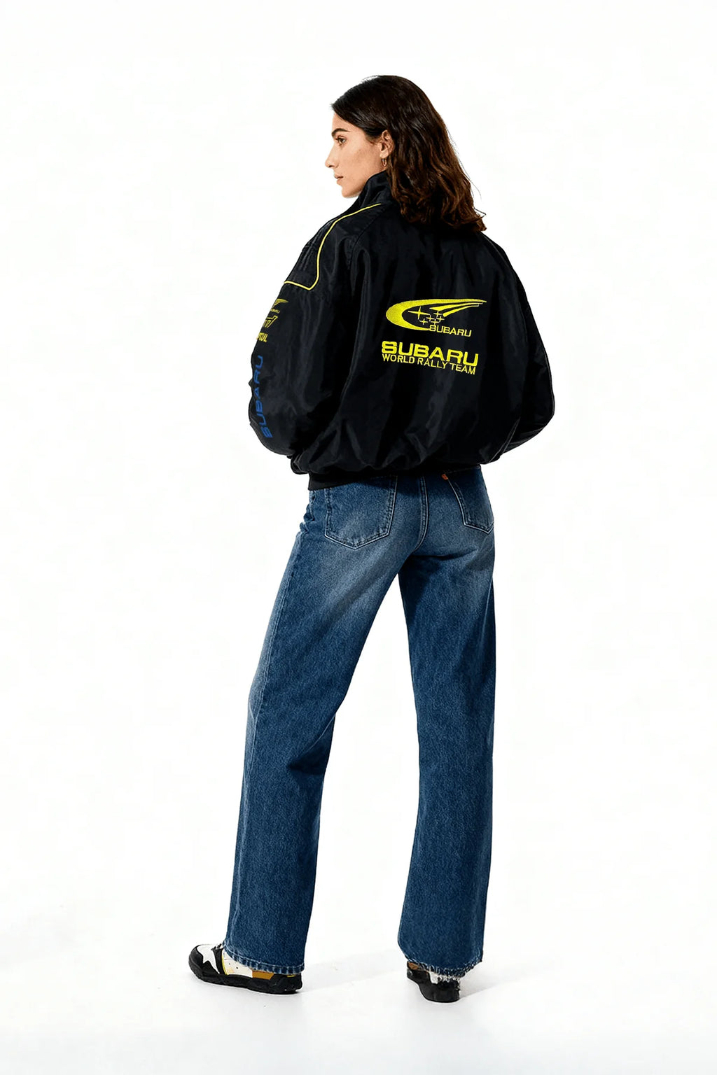 Black Subaru World Rally Team jacket with yellow logo, worn by woman in jeans, from revnhaus