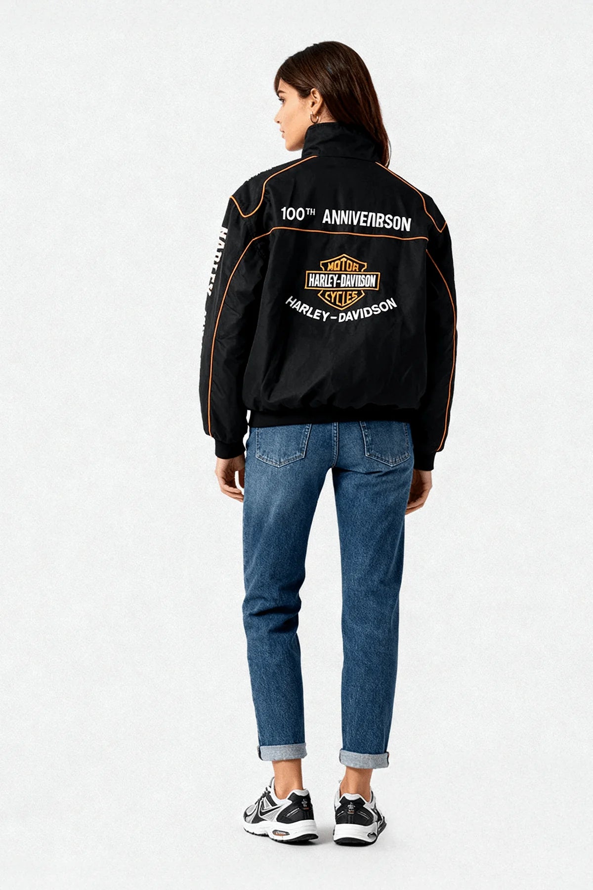 Black Harley-Davidson 100th Anniversary racing jacket with orange trim, worn by woman in jeans from revnhaus
